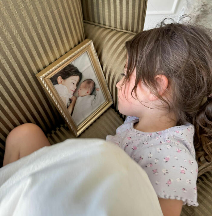 Young girl lying on a striped couch holding a framed photo of two sleeping children, reflecting on loss of influencer's daughter.
