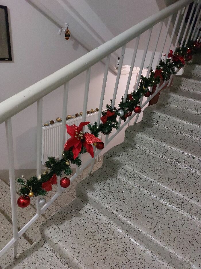 Christmas garland with red and gold ornaments decorating a stair railing in a Lithuanian apartment building.