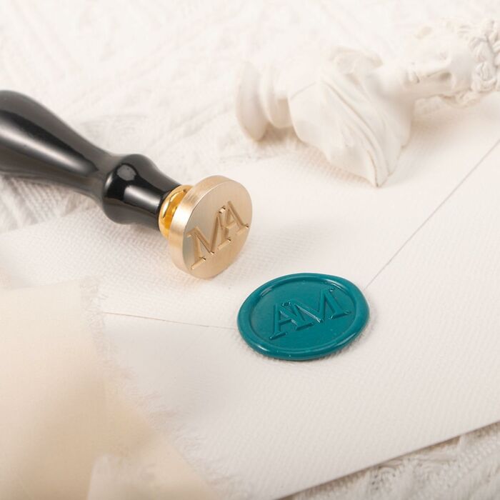 Wax seal stamp with AM initials and matching teal wax seal on white fabric, a stylish gift for mother-in-law gifts ideas.