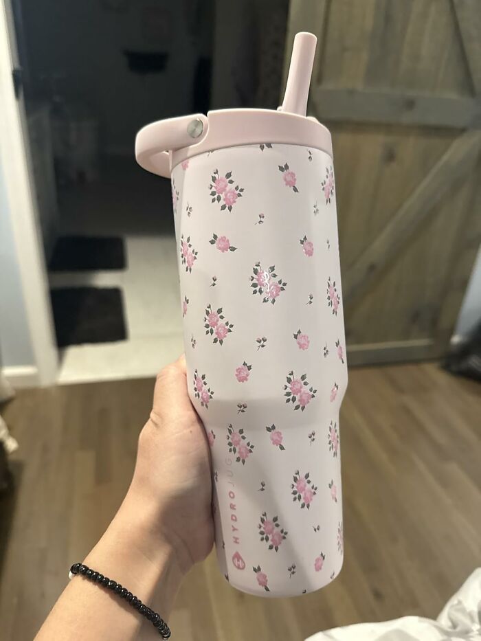Hand holding a pink floral Hydro Flask tumbler with a straw, a popular gift that teens are begging Santa for this year.