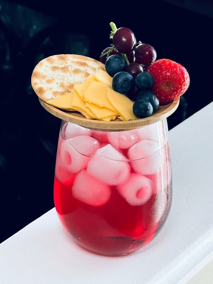 Cheese and fruit platter on wooden board over a glass of iced red drink as a useful present idea.