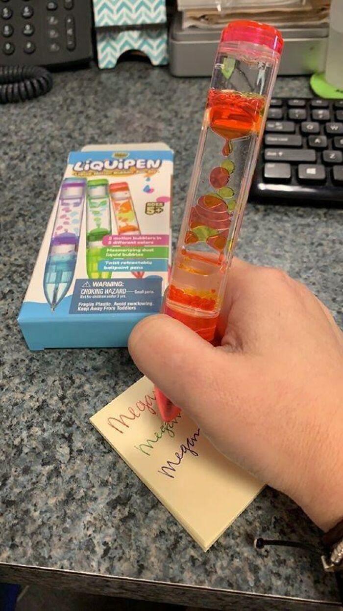 Hand holding a colorful liquid bubble pen writing on a sticky note, a unique white elephant gift idea on desk.