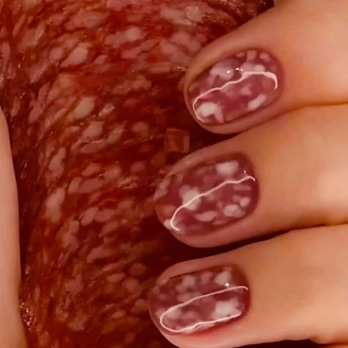Close-up of fingers with marbled nail art featuring red and white patterns, creating a trippy and surreal visual effect.