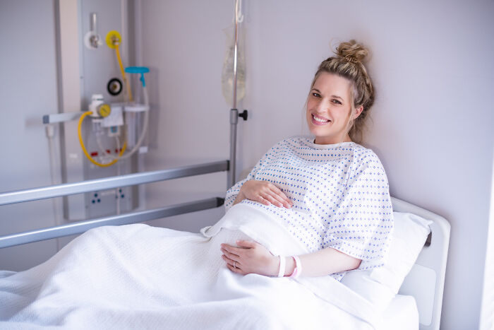 Pregnant woman in hospital bed smiling while waiting, illustrating men missed delivery babies experience.