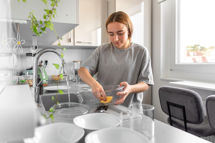 Young woman washing dishes in a bright kitchen demonstrating small tricks that make being a grown-up easier.