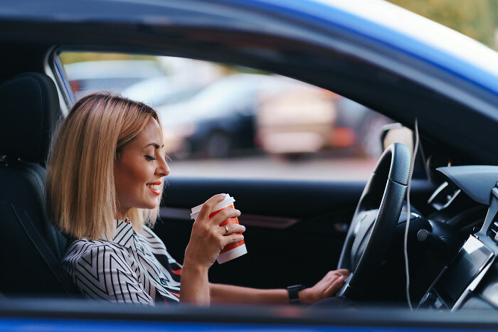 Woman smiling while sitting in a car holding a cup, a casual moment before unexpected big family drama unfolds.
