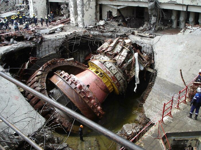 Massive industrial machinery partially submerged in water inside a damaged facility, evoking megalophobia fears.