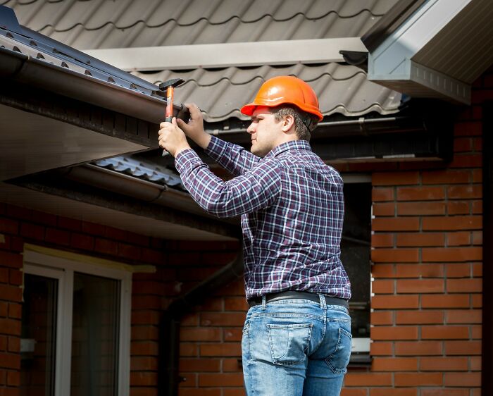 Man in orange hard hat and plaid shirt fixing gutter on house, an example of bizarre things seen through neighbor’s window