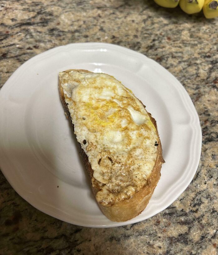 Fried egg perfectly aligned on a slice of toasted bread on a white plate on a granite countertop.
