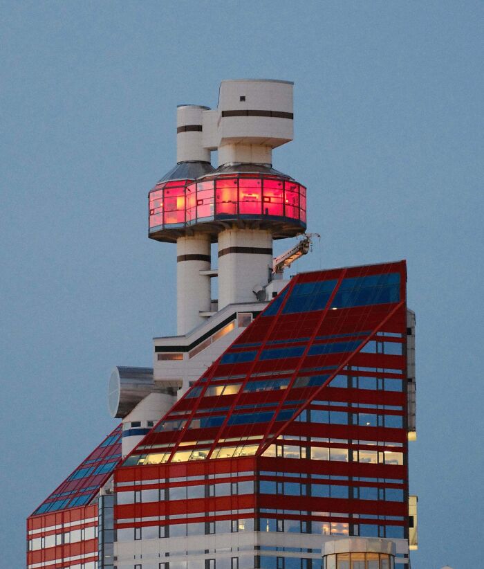 Unique bizarre building with glowing red windows and futuristic design standing against a clear evening sky.