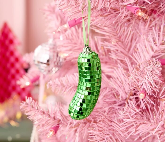 Green disco ball pickle ornament hanging on a pink Christmas tree with quirky gifts for unhinged taste.