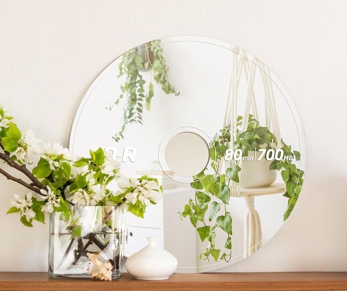 Round mirror designed as a giant CD reflecting a hanging plant and decor, a quirky gift for gloriously unhinged tastes.