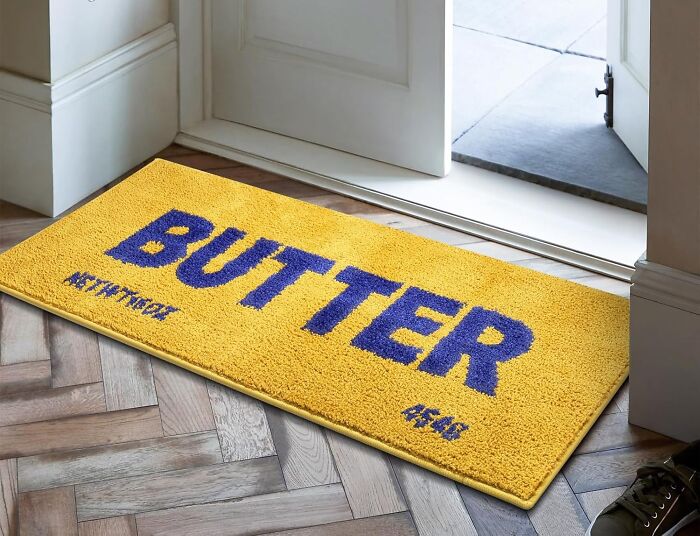 Yellow and blue quirky gift doormat with the word butter near an open white door on a wooden floor.