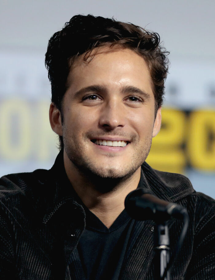 Diego Boneta smiling during a panel discussion, wearing a black jacket and speaking into a microphone at an event.