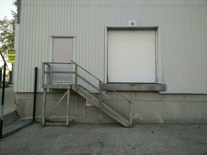 Wooden stairs lead to a sealed door next to a loading dock, showcasing poor job e*******n and design failure.