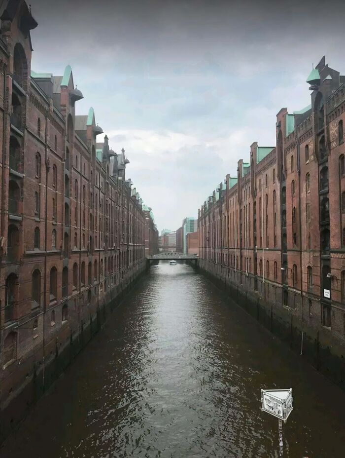 Evil buildings with dark brick facades lining a gloomy canal under a cloudy sky, evoking horror movie vibes.
