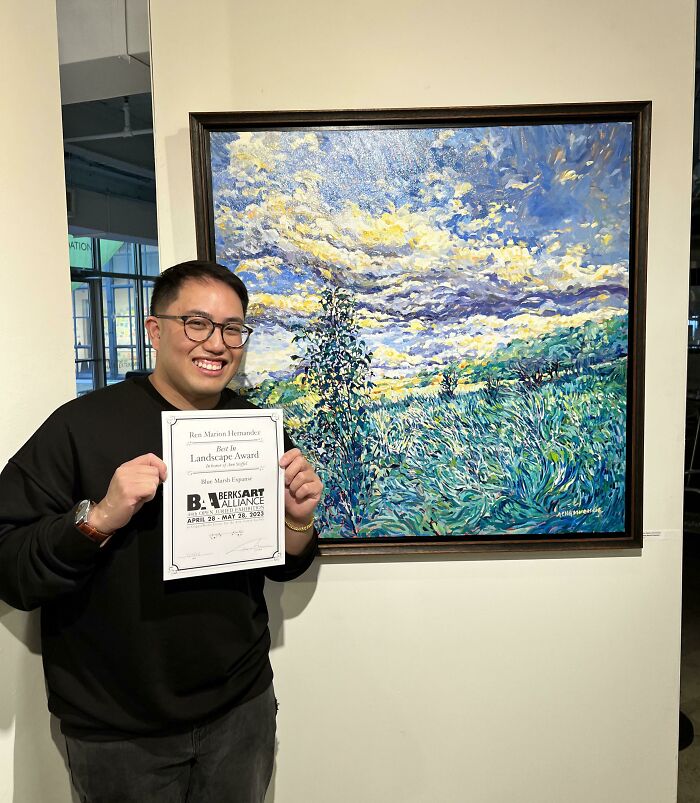 Young man proudly holding award next to vibrant landscape painting, illustrating moments people took a leap of faith.
