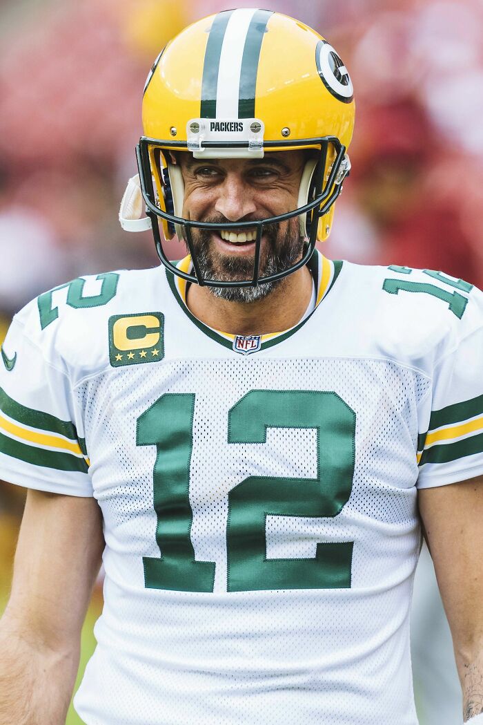 Aaron Rodgers smiling on the field wearing a Green Bay Packers helmet and jersey during an NFL game.