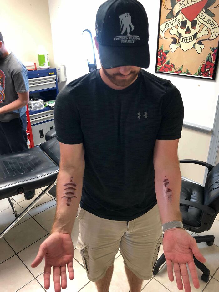 Man showing matching soundwave tattoos on both forearms in a tattoo studio, showcasing meaningful ink designs.