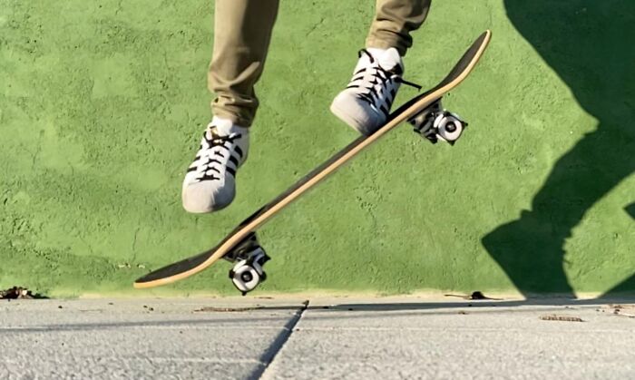 Person wearing white sneakers performing a skateboard trick on a green surface, popular products on Amazon wish lists.