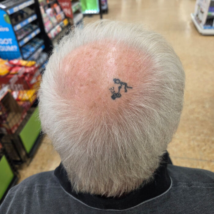Small wholesome tattoo of a stick figure hanging from a branch on the bald spot of an elderly man's head.