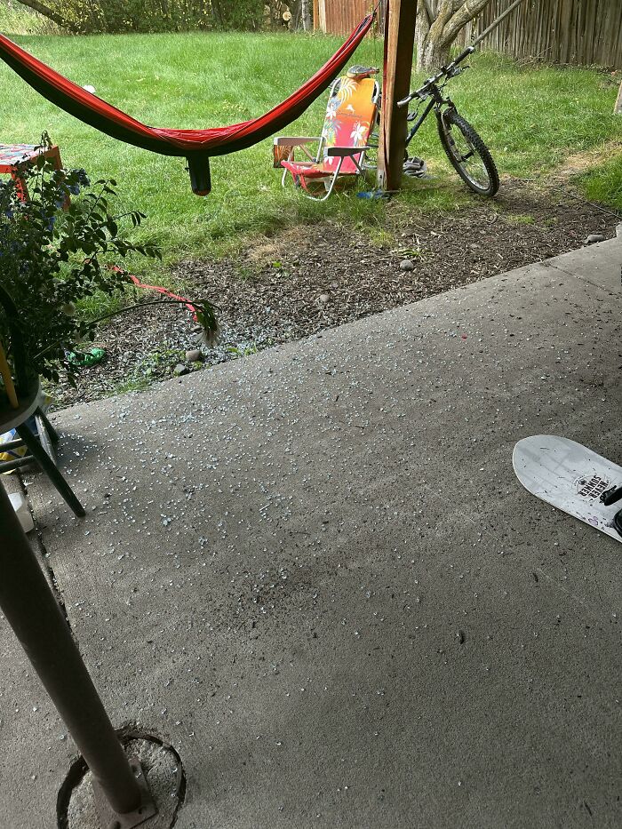 Backyard patio with broken glass scattered on the floor, a hammock, a bike, and a colorful lawn chair showing rental nightmares.