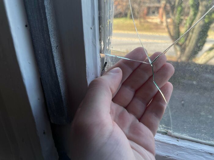 Hand inspecting c*****d window glass in a rental property showing landlord rental nightmares and corner-cutting mistakes.