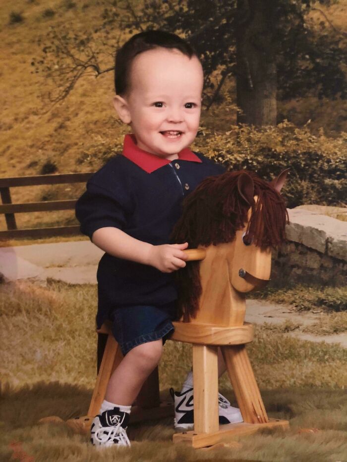 Toddler smiling while sitting on a wooden rocking horse in a playful and awkward childhood photo.
