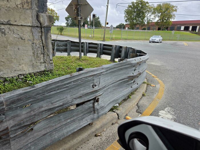 Rusty bent metal guardrail wrapping tightly around a corner creating a confusing visual effect for the brain to catch up.