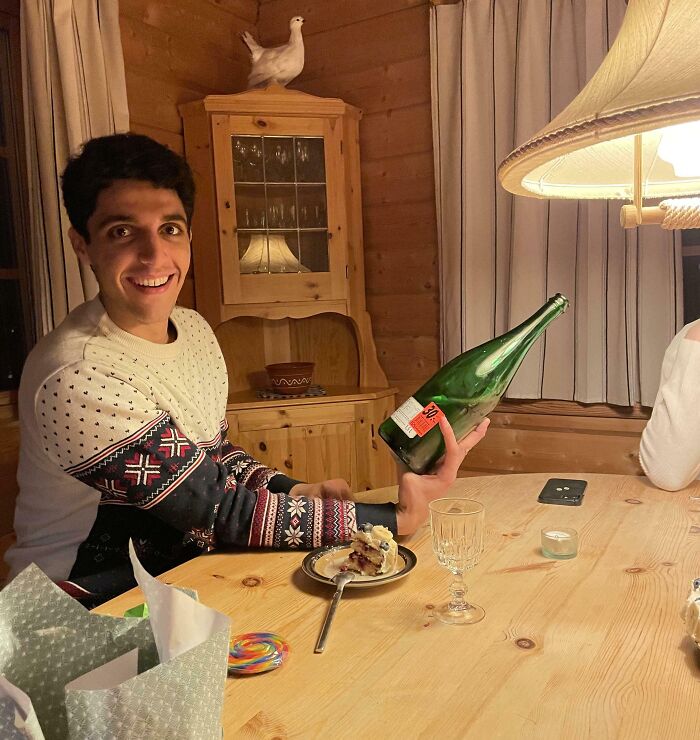 Young man in a cozy room holding a large green bottle at an angle, creating a confusing photo for the brain to catch up.