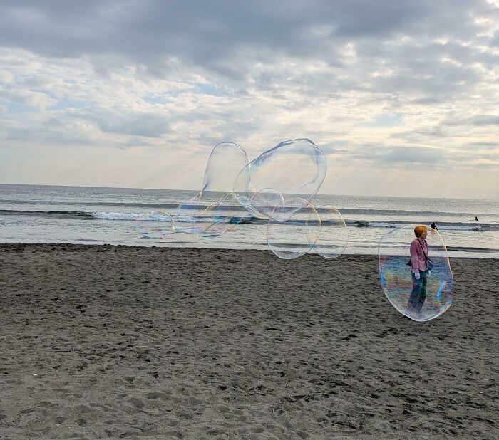 Person on beach inside giant transparent bubble, with several large bubbles floating above the sand, confusing photo effect.