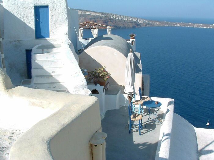 White and blue Mediterranean terrace overlooking the sea, with tiny cats hidden in big spaces nearby.