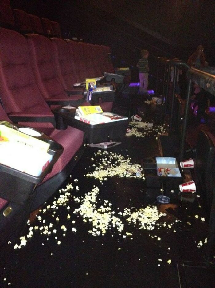 Messy movie theater aisle with spilled popcorn and discarded drink cups, a rage-inducing scene in a cinema setting.