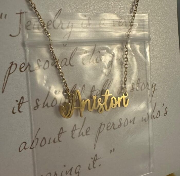 Gold custom name necklace with Aniston pendant displayed on a clear bag over handwritten gift note for Christmas.