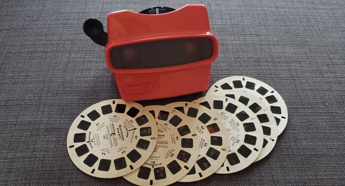 Red vintage View-Master toy with multiple photo reels on a gray fabric surface for custom gifts.