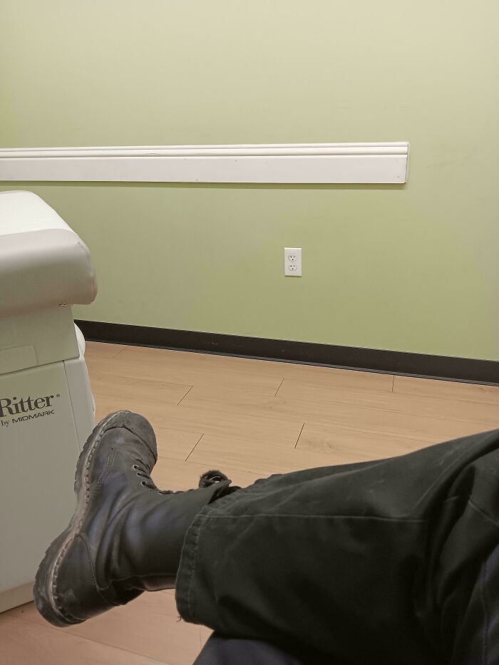 Patient's leg with worn black boot resting beside medical examination table in a calm clinical room setting.