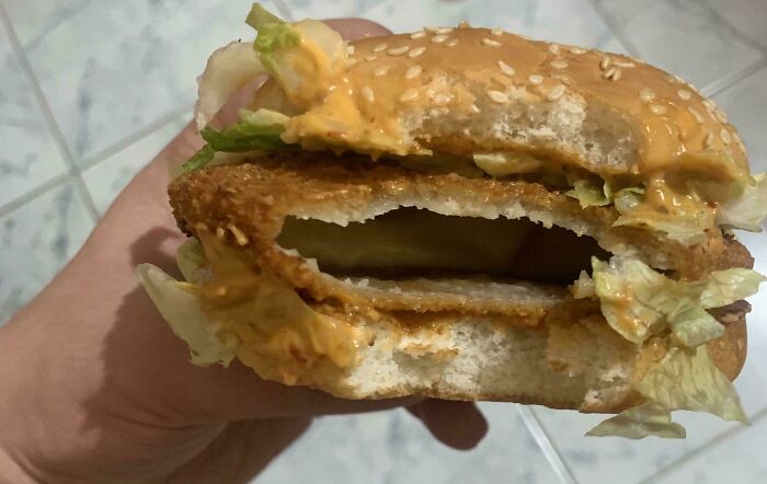 Partially eaten fish sandwich with lettuce and sauce, showing missing expected contents causing mild frustration.