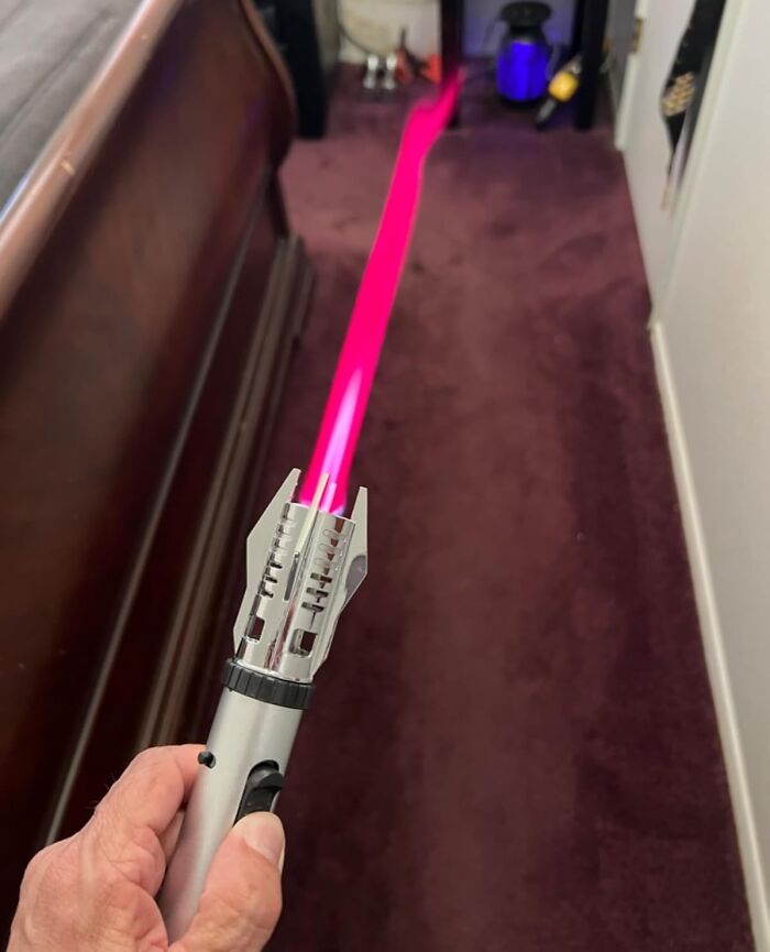 Hand holding a lightsaber toy glowing pink, a creative white elephant gift idea for festive gift exchanges.