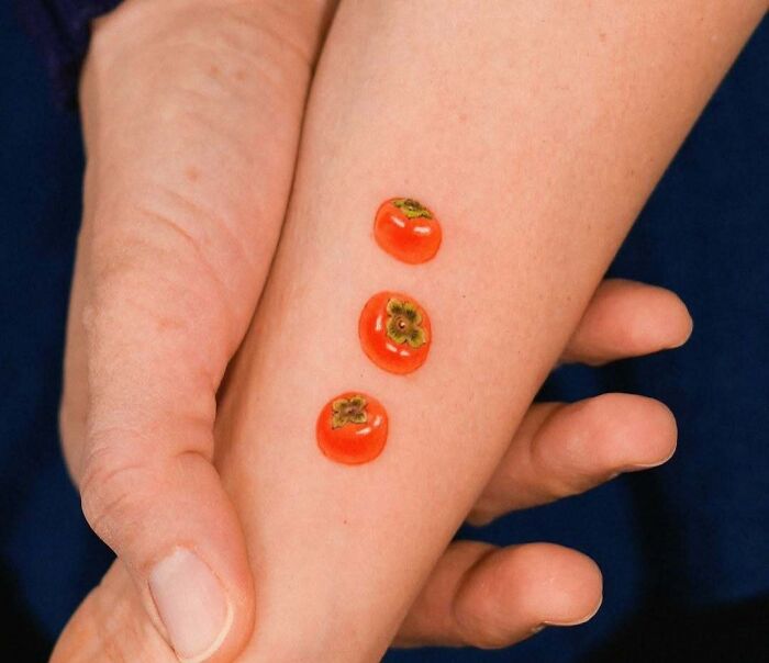 Small wholesome tattoos of three bright orange persimmons on inner forearm, showcasing meaningful ink art.