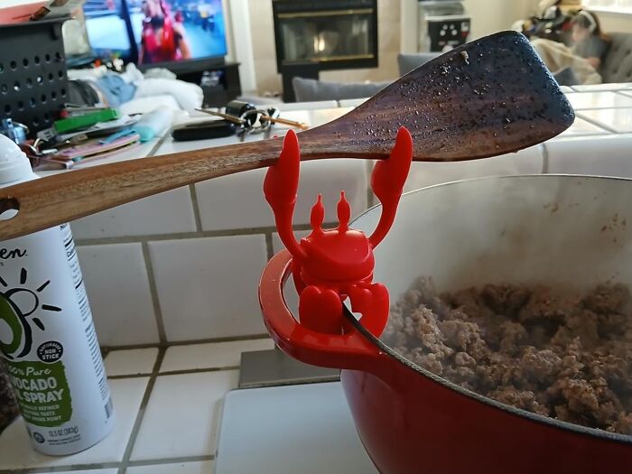 Red crab spoon holder balancing a wooden spatula on a pot of cooked ground meat, a quirky white elephant gift idea.