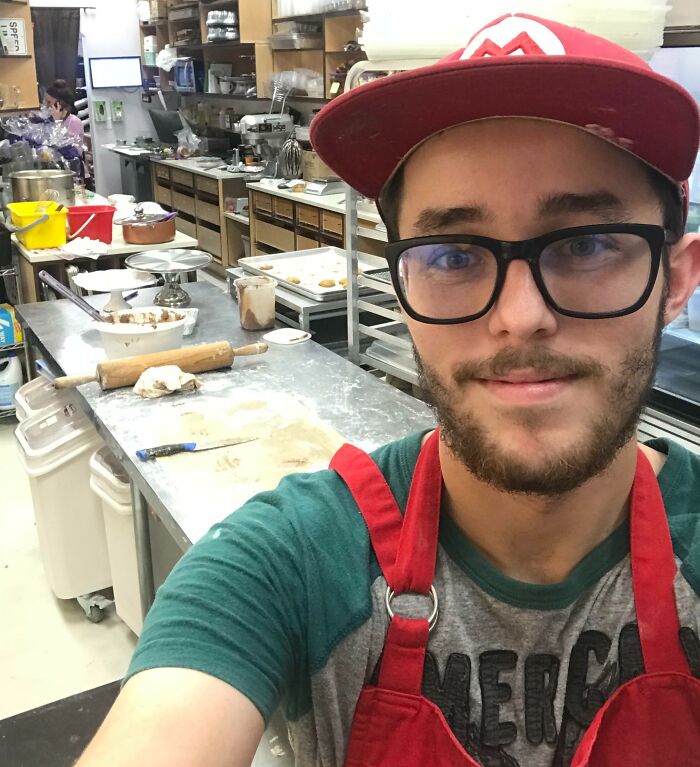 Young man wearing glasses and a red hat working in a bakery, showing confidence after taking a leap of faith.