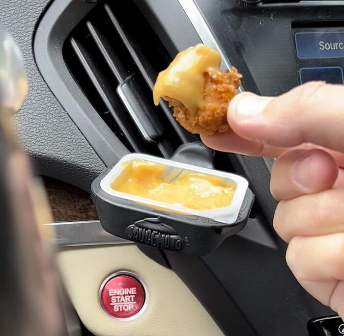 Hand dipping fried snack into sauce attached to a car vent, a unique white elephant gift idea for fun and practical use.