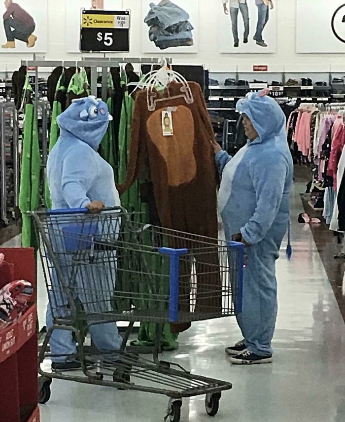 Two people in blue animal costumes shopping and holding a brown costume inside a Walmart store unusual scene.