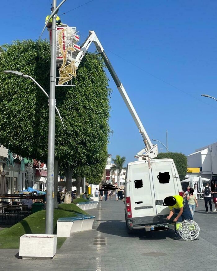 Worker fixing a streetlight decoration while a van is dangerously parked and the job appears poorly done in public space.