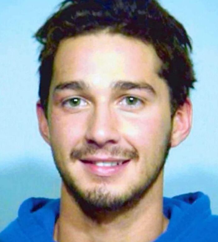 Young man with dark hair and green eyes wearing a blue hoodie in a celebrity mugshot after being arrested.