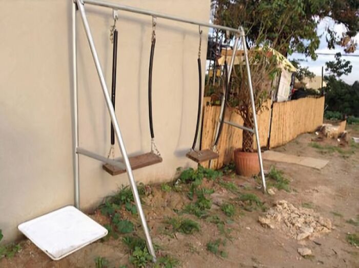 Swing set with one missing swing, two wooden swings, and uneven ground showing poor job e*******n.