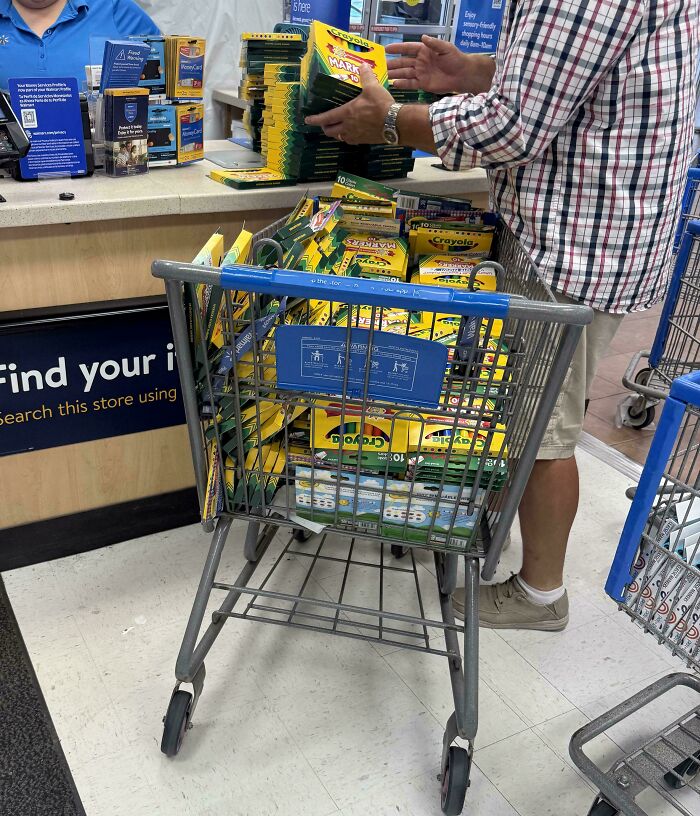 Customer at Walmart checkout with a cart full of Crayola markers and art supplies in a brightly lit store aisle.
