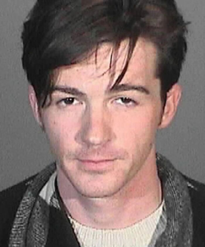 Young male celeb with dark hair in a casual shirt posing for a mugshot after being arrested in a celebrity mugshot collection.