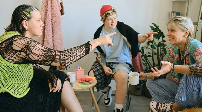 Three friends enjoying the best party game of all time, laughing and pointing while sitting in a cozy room.