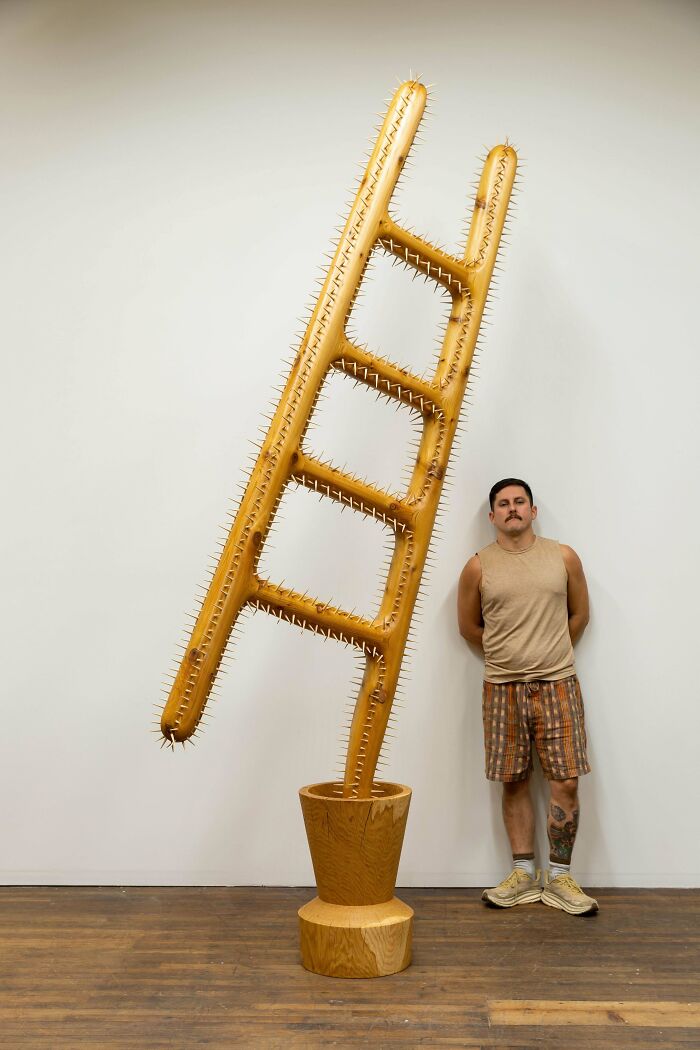 Man standing next to a large wooden sculpture resembling a spiked ladder, showcasing incredible woodworking projects.